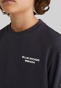 Mörkgrå våffelstickad sweatshirt med ribbad rund halsringning och "BLUE RIDGE DENIM"-logotyp i vitt på bröstet. Mjuk textur.