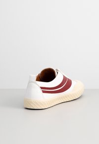 Baskets basses blanches avec semelle beige et deux bandes rouges sur le côté, vues de dos en angle.
