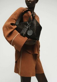 Borsa in pelle nera a forma triangolare, con una cerniera argentata, un charm rotondo, superficie liscia e manici robusti.