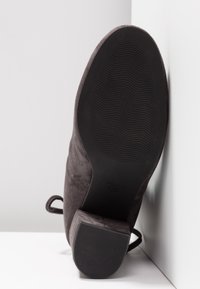 Vue de la semelle d'une botte cheville en suède foncé avec un petit talon épais et une semelle extérieure en caoutchouc texturé pour une meilleure adhérence.