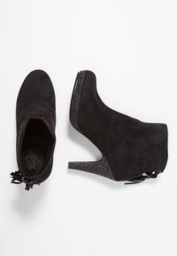 Bottines en suédine noire avec un bout pointu, un talon pailleté haut et un détail de nœud décoratif à l'arrière. Doublure douce à l'intérieur.