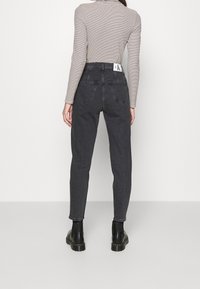 Černé džíny s vysokým pasem, slimový střih, pět kapes, jemné detaily prošití a logo štítek na zadním pasu, doplněné pruhovaným topem.