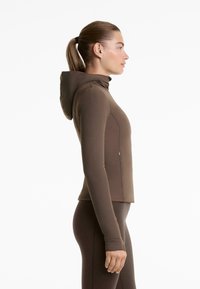 Rjava kapuca jakna iz raztegljivega materiala, slim fit kroja, z dolgimi rokavi in zadrgo na strani. Minimalističen dizajn.