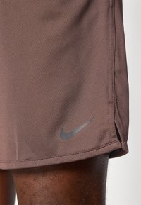 Brown athletic shorts with a textured fabric, side slits, and a black Nike logo near the hem.
