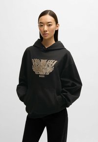 Svart hoodies med ficka framtill, prydd med ett guldemblem och texten "BOSS" ovanför intrikata mönster. Mjuk bomullsblandning.