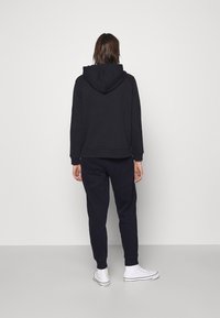 Ciemnogranatowa bluza z kapturem, kieszenią kangurzą i sznurkiem, zestawiona z dopasowanymi spodniami dresowymi. Oba elementy mają ściągacze przy mankietach oraz miękką fakturę.