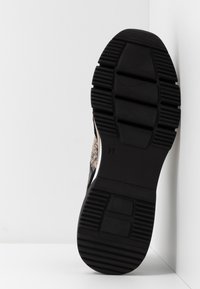 Semelle de sneaker en caoutchouc noir texturé, avec un dessus à motifs au design serpent. Taille 37 indiquée sur le côté.