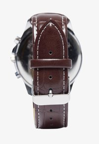 Correa de reloj de cuero marrón con acabado texturizado, costura blanca y hebilla de metal plateado. Presenta un extremo puntiagudo y agujeros de ajuste.