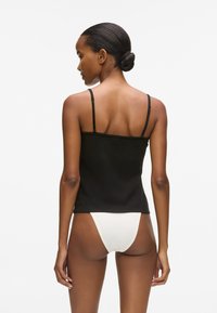 Melnas pieguļo�šas topiņš ar plānām siksnām, apvienots ar baltām augstām biksēm. Gluda tekstūra, vienkāršs dizains, bez redzamām rakstu vai akcentu detaļām.