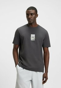 Camiseta gris de manga corta con cuello redondo, que presenta un logo impreso y acentos gráficos en la parte frontal. Confeccionada en tejido suave y ligero.