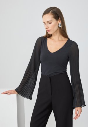Top negru cu maneci lungi plisate transparente si decolteu in V. Asortat cu pantaloni negri cu talie inalta pentru un siluetă elegantă.