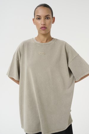 Oversized beige t-shirt made of soft cotton, featuring a round neckline, short sleeves, and a subtle logo embroidered at the front.