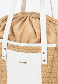 Beige gewebte Strohtasche mit weißen Kunstlederakzenten, runder Form, gerafftem oberen Teil und goldfarbenem Logo-Element. Glatte Textur und robuste Griffe.