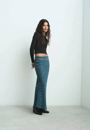 Dlhá smaragdová sukňa s kvetinovým vzorom a jemným leskom, kombinovaná s čiernym crop topom a čiernymi členkovými čižmami. Hladký, priliehavý silueta.