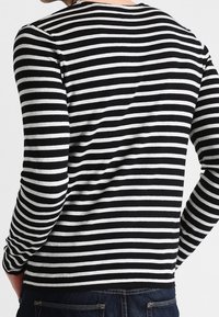 Pull à manches longues rayé noir et blanc avec un col rond, présentant une coupe ajustée et une texture douce. Tissu en coton texturé.