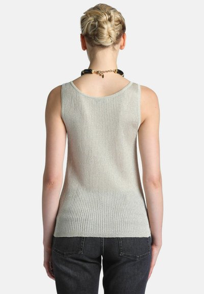 Femme avec un chignon tressé portant un haut gris clair côtelé sans manches et un jean noir, vue de dos sur un fond uni.