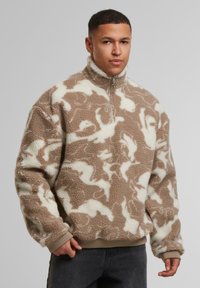 Pullover in pile marrone e crema con colletto alto, chiusura con zip e motivo astratto. Presenta polsini e orlo a coste, tessuto morbido.