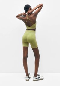 Brassière de sport côtelée vert olive avec bretelles croisées, associée à un short taille haute assorti, portée avec des baskets blanches à accents noirs.