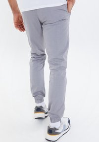Hellgraue tapered Pants aus weichem Stoff, mit elastischen Bündchen und seitlichen Taschen, kombiniert mit mehrfarbigen Turnschuhen.