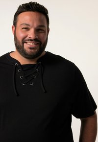 Černé tričko s krátkým rukávem s vlečným výstřihem a kovovými kroužky. Měkká tkanina s hladkým povrchem. Úzký střih.