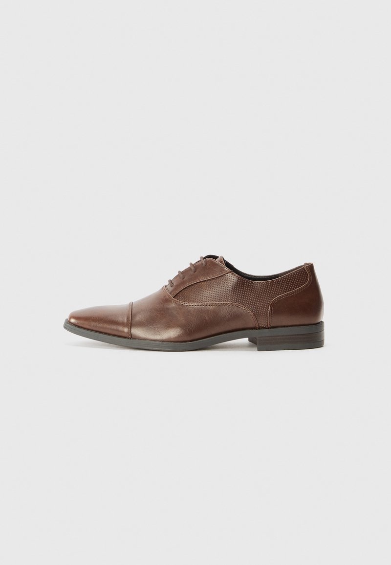 Chaussure habillée en cuir marron pour homme avec lacets, bout pointu et petit talon sur un fond uni clair.