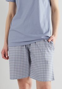 T-shirt azzurro chiaro abbinato a pantaloni corti a quadretti con tonalità di blu, bianco e rosa chiaro. I pantaloni corti hanno tasche laterali e una vestibilità comoda.