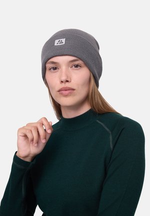 Bonnet en tricot gris avec un rebord replié et un patch logo. Porté avec un haut à col montant vert foncé. Texture lisse, ajustement confortable, design décontracté.