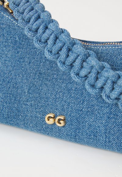 Denim håndtaske med flettet strop, lys blå farve, guld hardware accenter, glat tekstur og lynlås lukning. Har to runde nitter.