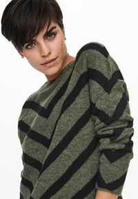 Grüner Strickpullover mit schwarzen Chevronstreifen, rundem Ausschnitt und langen Ärmeln mit umgeschlagenen Bündchen. Weicher Griff und entspannte Passform.
