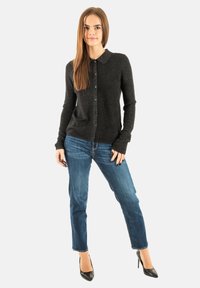 Cardigan nero a maniche lunghe con colletto e chiusura a bottoni, abbinato a jeans blu e tacchi alti neri. Tessuto morbido.