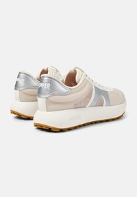 Zapatillas beige con parte superior de malla y sintético, acentos plateados y una suela blanca gruesa. Suela de goma texturizada para un mejor agarre.