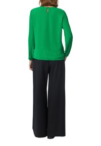 Blouse verte avec des manches plissées, dos en goutte d'eau, associée à un pantalon noir à jambe large. Tissu lisse, design simple sans embellissements.