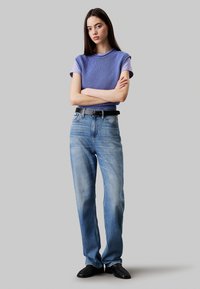 Top sin mangas de punto púrpura con cuello redondo, combinado con jeans de pierna recta de color azul claro y un cinturón negro. Textura suave y ajuste casual.