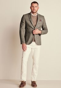 Grau melierter Blazer über einem beigen Pullover, weiße Hosen und braune Schuhe. Merkmale sind ein Taschentuch, ein strukturiertes Design und ein strapazierfähiger Stoff.