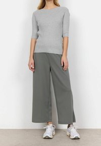 Szary prążkowany top z krótkimi rękawami do łokci w połączeniu z szerokimi oliwkowymi spodniami. Sneakery w białym i jasnoszarym kolorze.