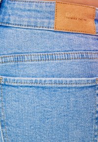 Ljusblå denimjeans med textilerad yta, med en läderlapp märkta "Bershka Est. 98" på midjebandet.