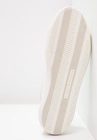 Vit sneakersula med texturerade gummimönster, med en slät yta och "TOMMY HILFIGER"-logotyp präglad nära kanten.