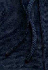 Gros plan sur un tissu texturé bleu foncé avec deux cordons torsadés se terminant par des embouts en plastique noir.