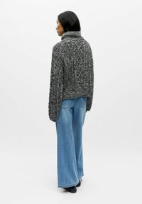 Chunky strikkegenser i svart og grått med høy krage, teksturert mønster og løs passform, kombinert med vide blå jeans.