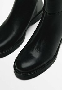 Black leather ankle boots with a rounded toe, smooth texture, minimal stitching, and a low, chunky heel.