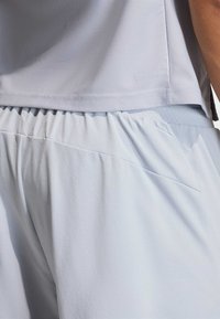 Light blue athletic top made of textured fabric, with a relaxed fit and waistband detail. Includes moisture-wicking technology for comfort.