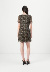 Robe noire avec manches courtes transparentes, motif floral en beige et marron, jupe évasée, coupe au genou, portée avec des sandales à talons noires.