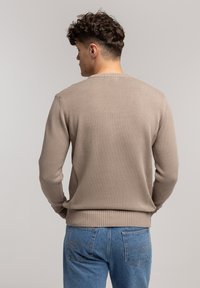 Jasnobrązowy sweter z dzianiny z okrągłym ściągaczem i ściągaczami na rękawach. Tył ma gładką fakturę i dopasowany kroj.