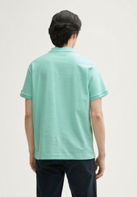 Koszulka polo z krótkim rękawem w jasnym miętowym kolorze, z subtelnym wzorem teksturowym oraz standardowym kołnierzykiem. Widok z tyłu nie pokazuje żadnych logo ani akcentów.