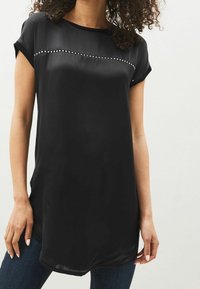 Sort silken blouse med korte ærmer, der har en vandret række af dekorative nitter over brystet. Glat tekstur og afslappet pasform.