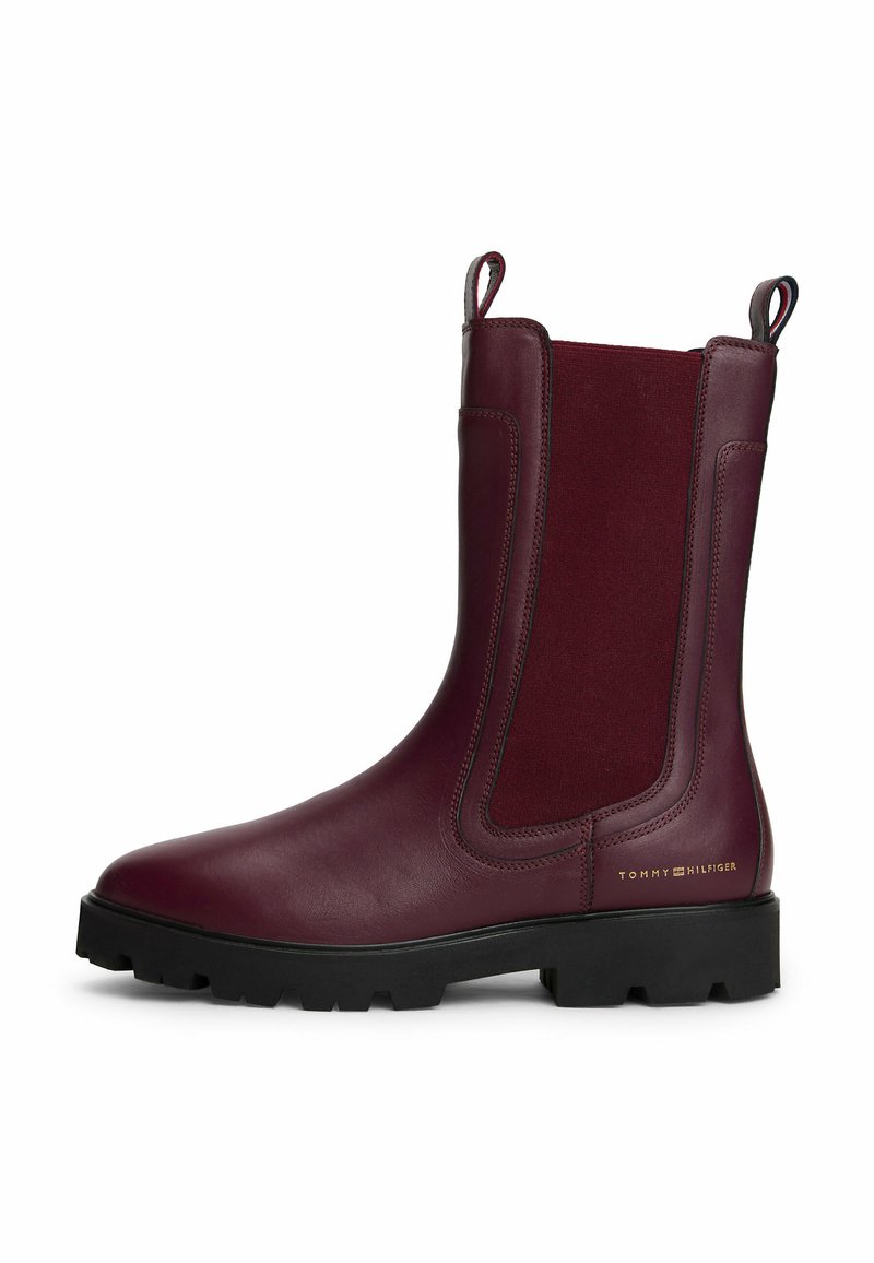 Botines Chelsea de cuero burdeos oscuro para mujer con suela negra de tacos, paneles laterales elásticos, tiradores y logo dorado de Tommy Hilfiger cerca del talón.