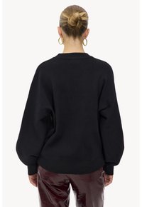 Pull noir oversize avec un ourlet côtelé et des manches larges, en matière tricotée. Le dos présente un design simple et épuré.
