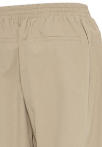Pantalon beige à taille élastique avec deux poches arrière à passepoil horizontales et une coupe ample.