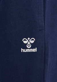 Granatowe dresy z białym logo stylizowanej pszczoły oraz napisem "hummel", wykonane z miękkiego materiału z mieszanki bawełny, o gładkiej fakturze.