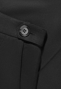 Fekete szövet sima felülettel, négylyukú gombbal és tiszta varrással az élen.